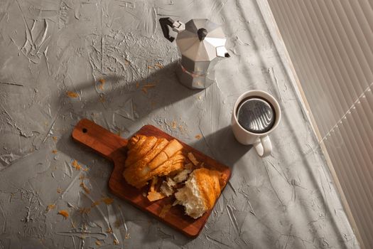 Breakfast with croissant on cutting board and black coffee. Morning meal and breakfast.