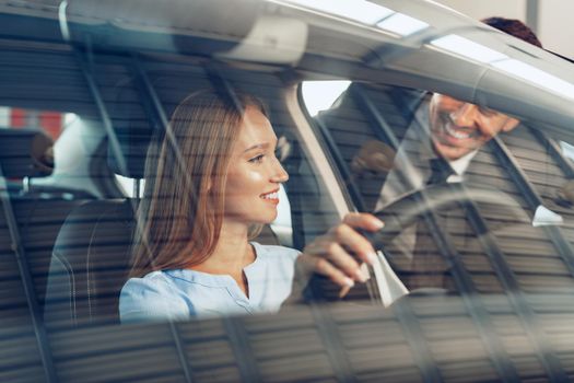 Attractive young woman sitting in new car in showroom close up