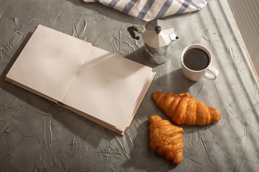 Breakfast with croissant and coffee moka pot and book with empty pages place for advertising. Morning meal and breakfast concept. Top view. Mockup.