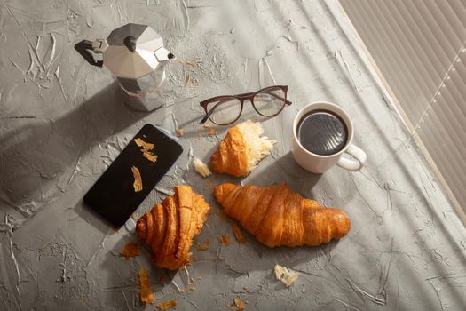 Breakfast with croissant on cutting board and black coffee. Morning meal and breakfast.