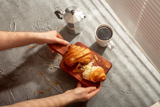 Breakfast with croissant on cutting board and black coffee. Morning meal and breakfast.