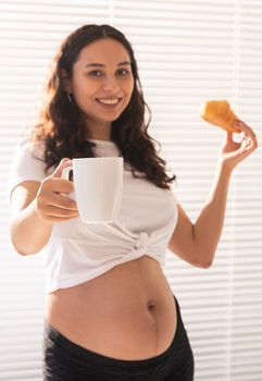 Happy pregnant woman with croissant buns at home. Pregnancy, eating and people