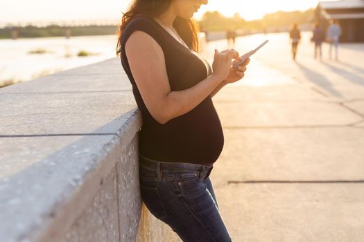 Close-up of pregnant woman with smartphone at park. Pregnancy, technology and communication
