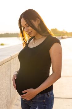 Portrait of a happy pregnant woman looking at side walking in a park at sunset. Pregnancy and motherhood