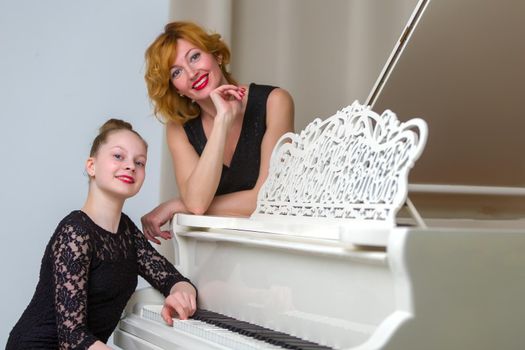 A beautiful young mother with a little daughter near a large white grand piano. The concept of family happiness, music education.