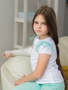 Child with a cast on a broken wrist or arm sits on a couch. Recovery and kid concept