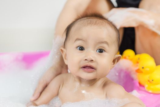 baby taking a bath in bathtub and playing with foam bubbles at home