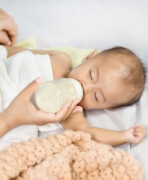 hand of mother feeding milk from bottle and baby sleeping on bed.