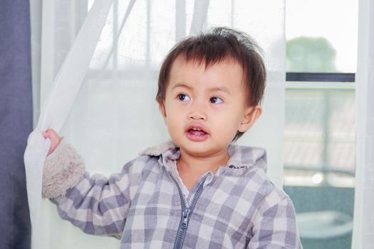 baby playing hide and seek behind the curtain at home