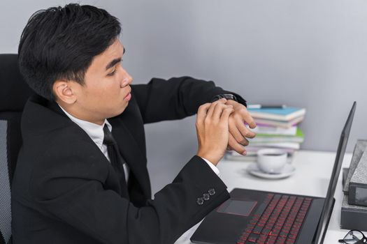 young business man checking time on watch while using laptop