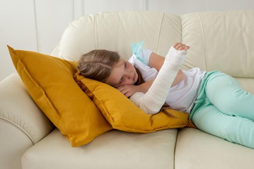 Child with a cast on a broken wrist or arm lying on a couch. Recovery and kid