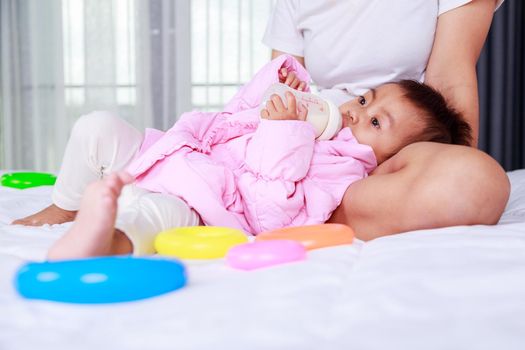 baby drinking a milk from bottle with mother on a bed