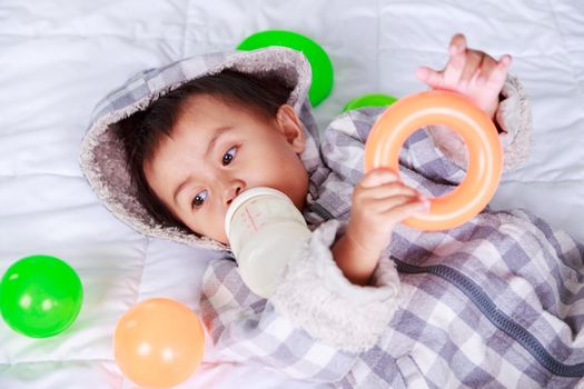 baby drinking milk with bottle on bed at home