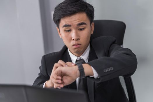 young business man checking time on watch while using laptop