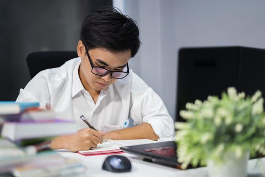 young man studying and writing on notebook with laptop computer