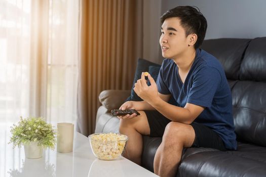 young man eating popcorn while sitting on a couch at home and watching TV