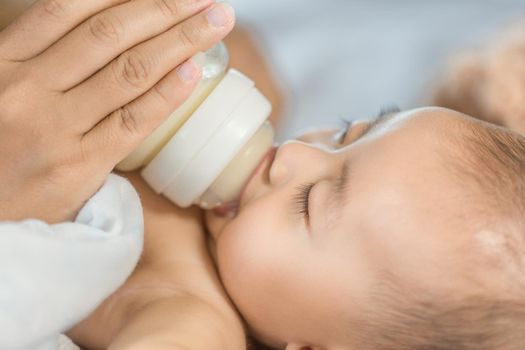 hand of mother feeding milk from bottle and baby sleeping on bed.