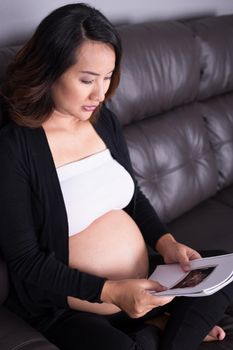 Pregnant woman sitting on sofa and holding her child ultrasound picture