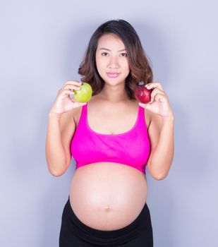 Beautiful pregnant woman with red and green apple on gray background