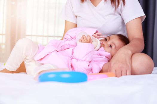 baby drinking a milk from bottle with mother on a bed