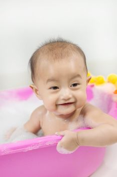 baby taking a bath in bathtub and playing with foam bubbles at home