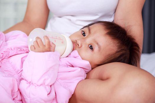 baby drinking a milk from bottle with mother on a bed