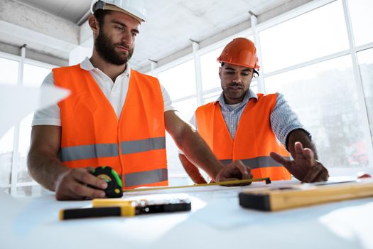 Two young engineers man looking at project plan on the table in construction site