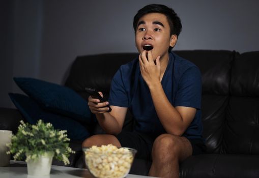 Shocked young man watching at tv and sitting on sofa in the living room at night