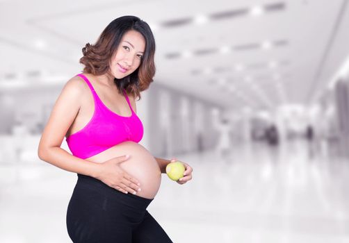 Beautiful pregnant woman with green apple in hospital background