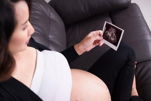 Pregnant woman sitting on sofa and holding her child ultrasound picture