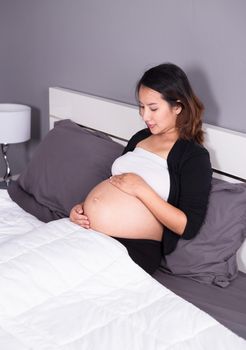pregnant woman looking at her belly while lying on the bed