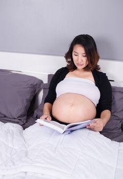 pregnant woman reading a book while lying on a bed in the bedroom at home