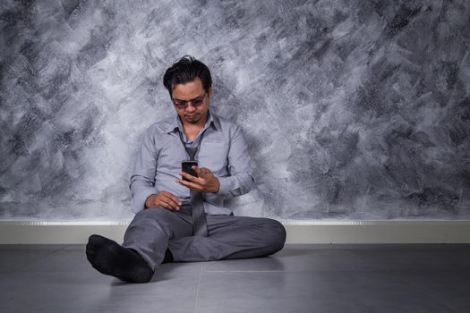 young depressed businessman with mobile phone and sitting on the floor 