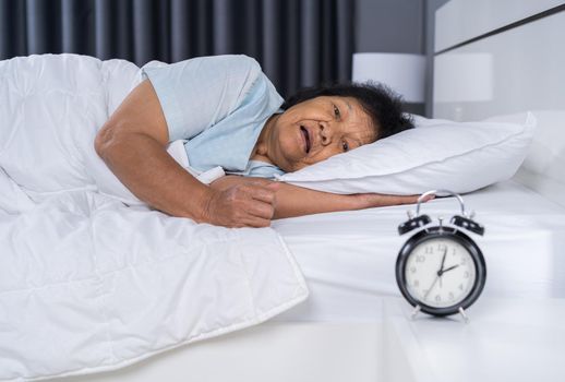 Old woman suffering from insomnia is trying to sleep in bed at night