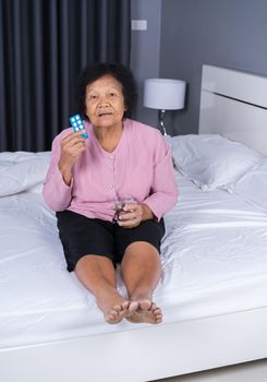 senior woman taking pill with glass of water in a bed