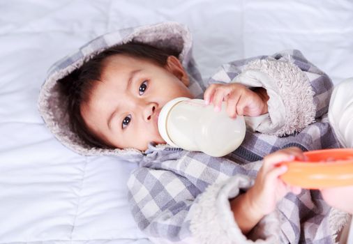 baby drinking milk with bottle on bed at home