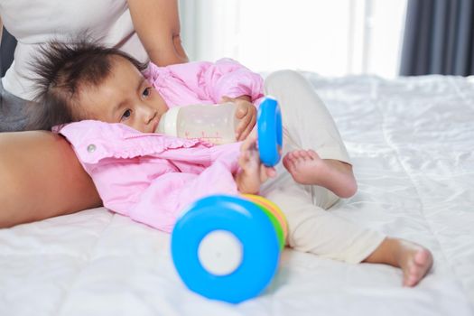 baby drinking a milk from bottle with mother on a bed