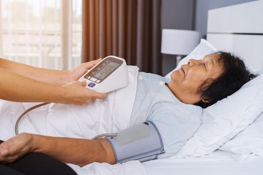 female nurse checking blood pressure of a senior woman on bed