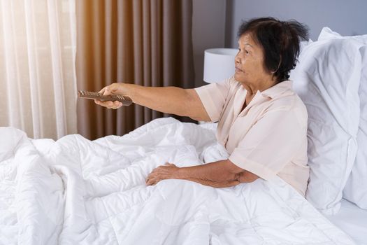 happy senior woman in bed with remote control and watching tv