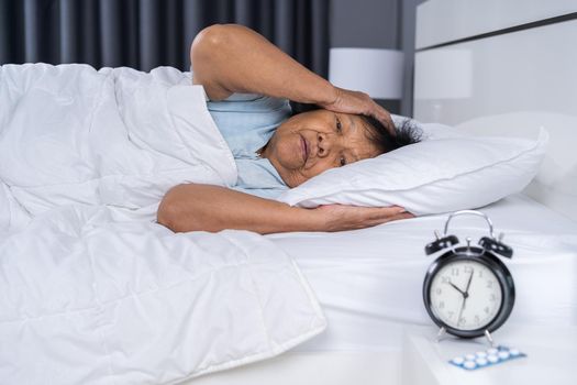 Old woman suffering from insomnia is trying to sleep in bed at night