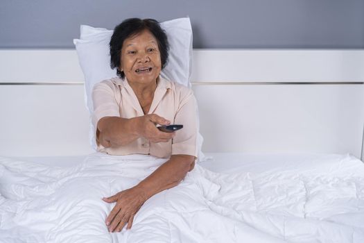 happy senior woman in bed with remote control and watching tv