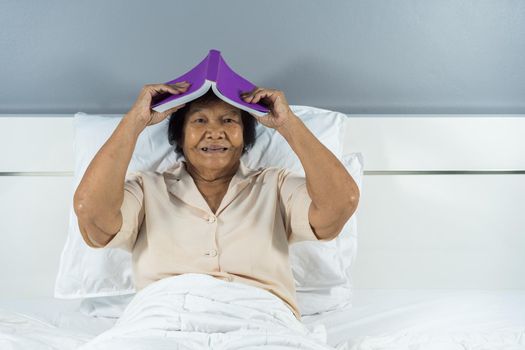 happy old woman in bed holding a book on her head