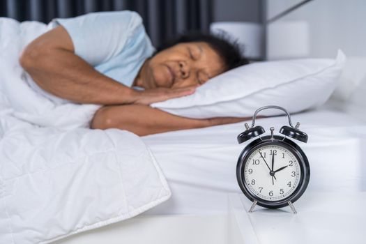 senior woman sleeping on a bed with a clock