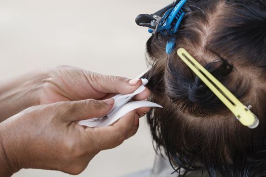 hand of a hairstylist doing a perm rolling the hair of senior woman