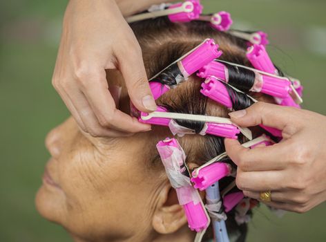 hand of a hairstylist doing a perm rolling the hair of senior woman