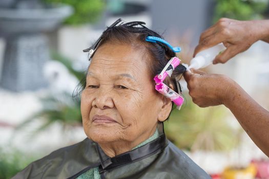 hand of a hairstylist doing a perm rolling the hair of senior woman