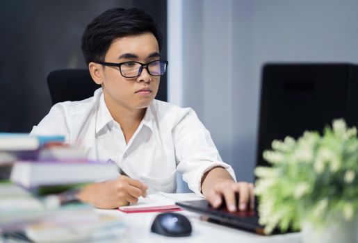 young man studying and writing on notebook with laptop computer