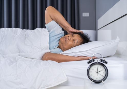 Old woman suffering from insomnia is trying to sleep in bed at night