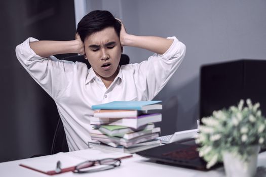 tired student sitting at the table with book and laptop