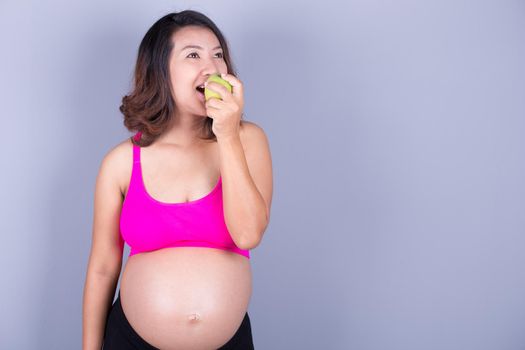 Beautiful pregnant woman with green apple on gray background